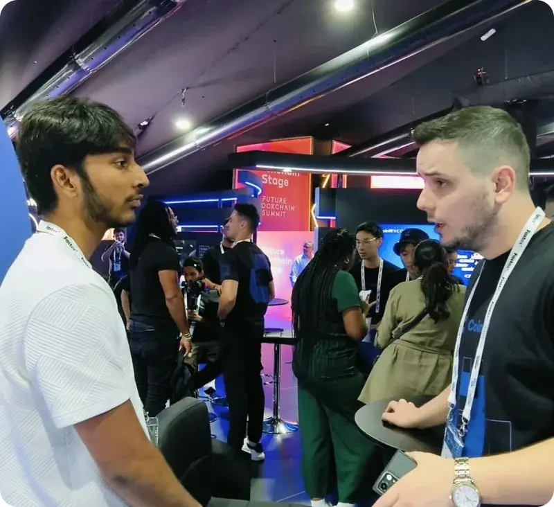 Nikesh speaking with another attendee in a busy indoor event space.