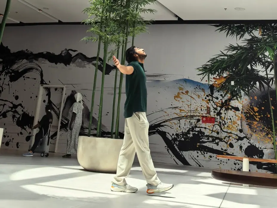 Nikesh looking upward as he walks beside tall bamboo in a sunlit indoor space.